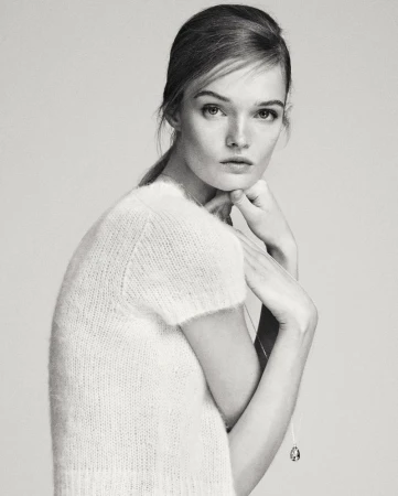 Monochrome portrait of model Lulu Tenney wearing a textured short-sleeve top and a delicate pendant necklace against a light background.