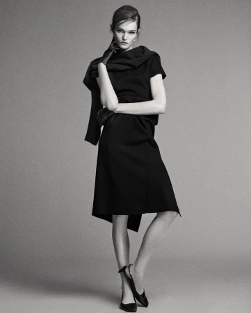 A full shot captures a woman posing in a black dress, gloves and shoes against a grey backdrop in a fashion photography studio setting.