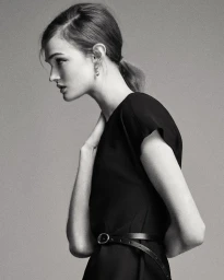 Monochrome fashion portrait of model Lulu Tenney in a black belted dress against a grey studio backdrop.