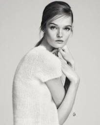 Monochrome portrait of model Lulu Tenney wearing a textured short-sleeve top and a delicate pendant necklace against a light background.