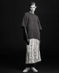 Model Lulu Tenney wearing a grey knit top and printed skirt with long black leather gloves against a black background