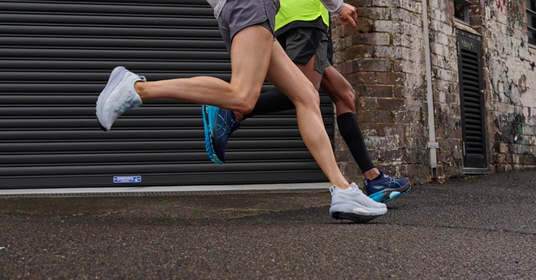Two runners in motion wearing athletic apparel and running shoes on an asphalt surface, with a metal roller door in the background.