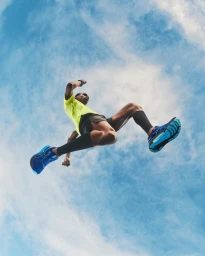 Runner in a bright yellow t-shirt and blue running shoes leaping against a clear blue sky
