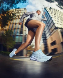 Low-angle action shot of a runner in athletic apparel sprinting through city buildings with radial motion blur.