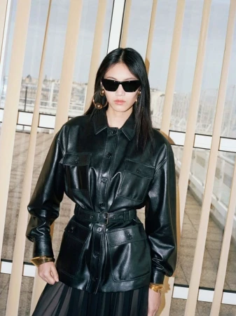 An Asian woman poses in a belted black leather jacket and sunglasses, showcasing a fashion-forward look against a neutral background.
