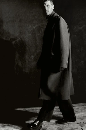 Model Clement Chabernaud in a dark coat walking against a textured background for Zara Man.