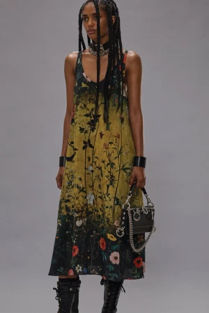 Model in printed floral dress with black handbag and dark boots against a grey studio backdrop
