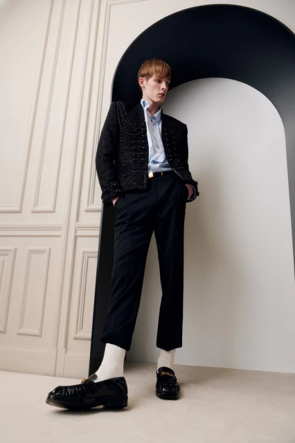 Male fashion model in tweed jacket, dress shirt, and slacks poses in front of an architectural backdrop for a studio portrait.