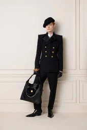 Model in a black double-breasted jacket and beret holding a large black leather handbag against a paneled wall