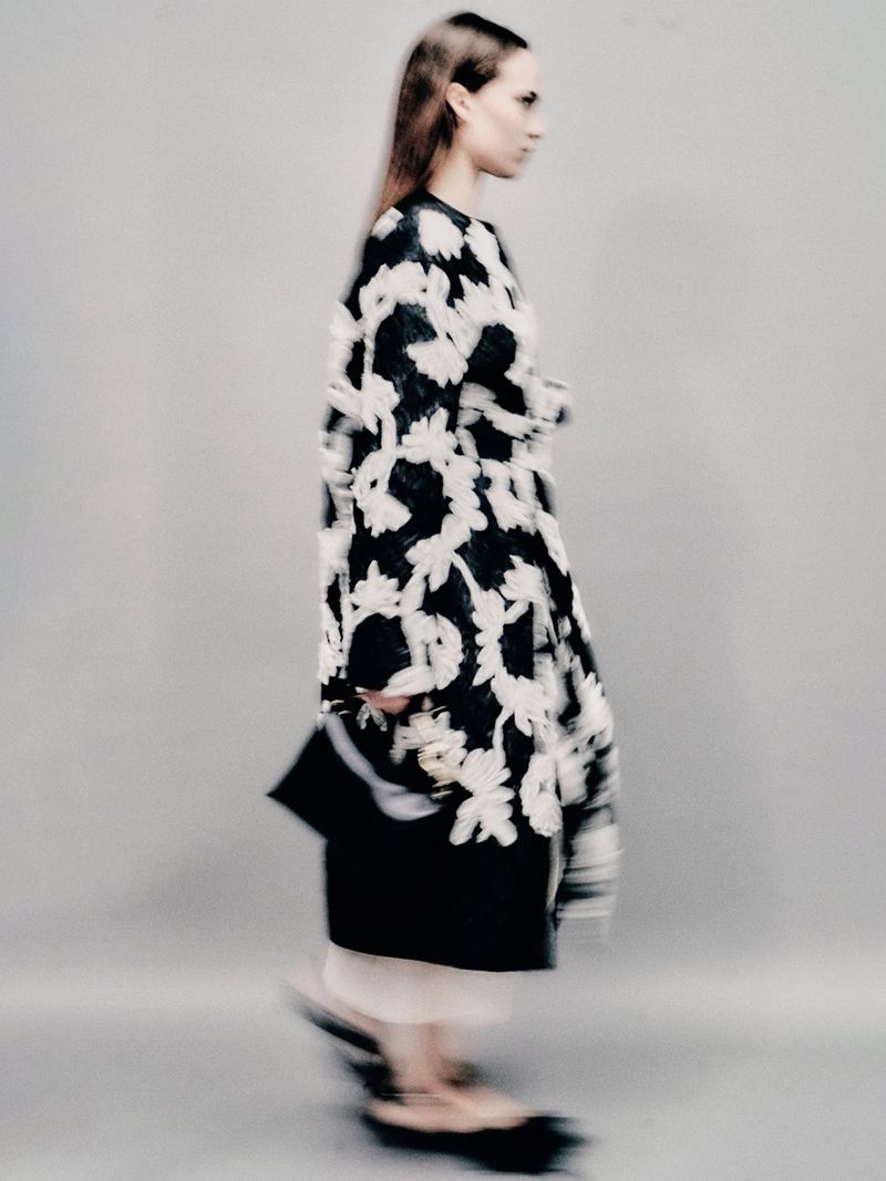 Fashion model showcases a black and white floral-print coat with black heels in a studio setting, captured with a motion blur effect.