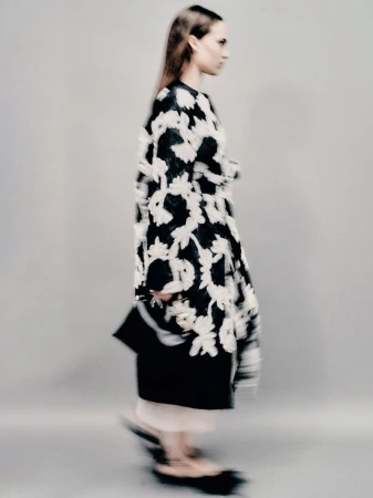 Fashion model showcases a black and white floral-print coat with black heels in a studio setting, captured with a motion blur effect.