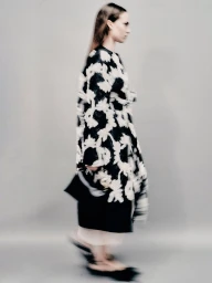 Model wearing a black and white patterned coat against a grey studio seamless background.