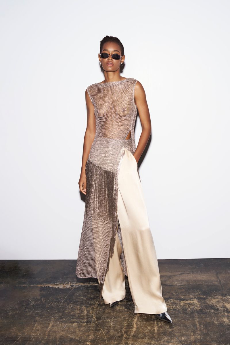 An adult female model poses in a sleeveless metallic top and satin pants against a white background, wearing sunglasses and minimalist jewelry.