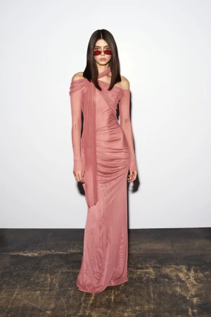 Model wearing a dusty rose halter neck long dress and red sunglasses standing against a plain white studio wall