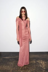 Model wearing a dusty rose halter neck long dress and red sunglasses standing against a plain white studio wall