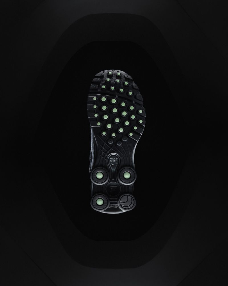 Sole of a black athletic shoe with green accents in a dark studio shot, highlighting the design and texture against a black background.