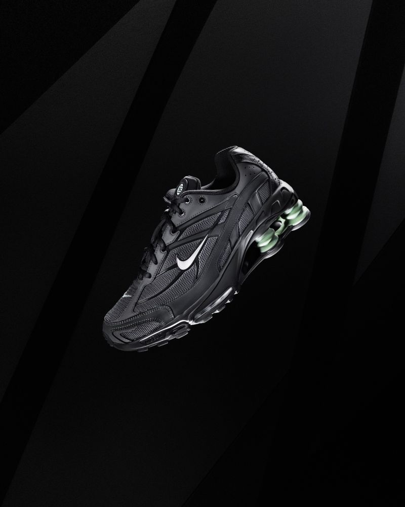 Studio shot of a black Nike sneaker, with a white swoosh, set against a gradient black backdrop with arcing light highlights.