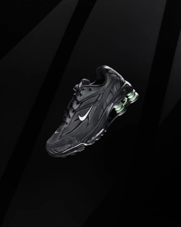 Studio shot of a black Nike sneaker, with a white swoosh, set against a gradient black backdrop with arcing light highlights.