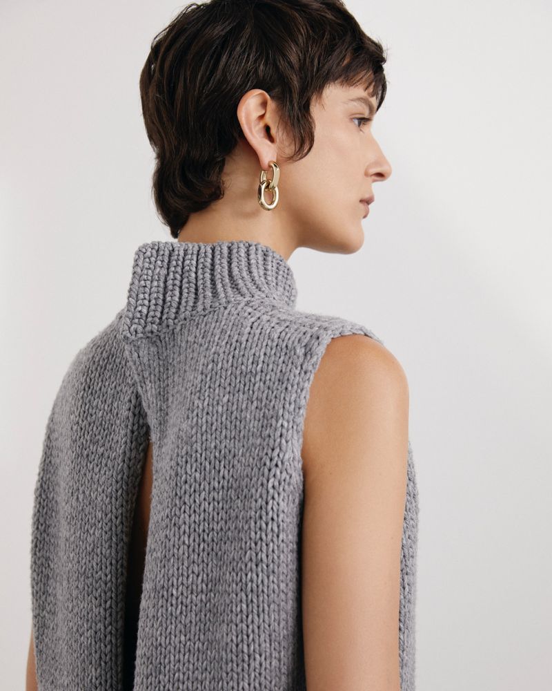 Profile view of a short-haired model wearing a sleeveless grey knit top and gold link earrings against a light background