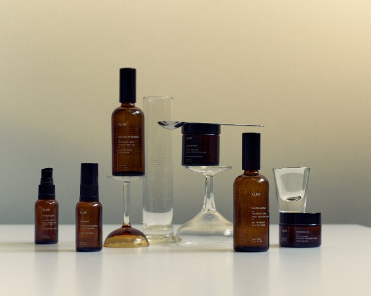 Still life shot of Klur skincare products in brown glass containers and vials, arranged on a white surface with reflective quality.