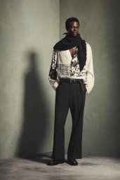 Model standing against a corner wall wearing a patterned white shirt and black trousers for Zara