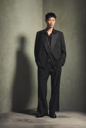 Man wearing a black suit jacket and matching trousers standing against a textured green studio wall for Zara Midnight Script