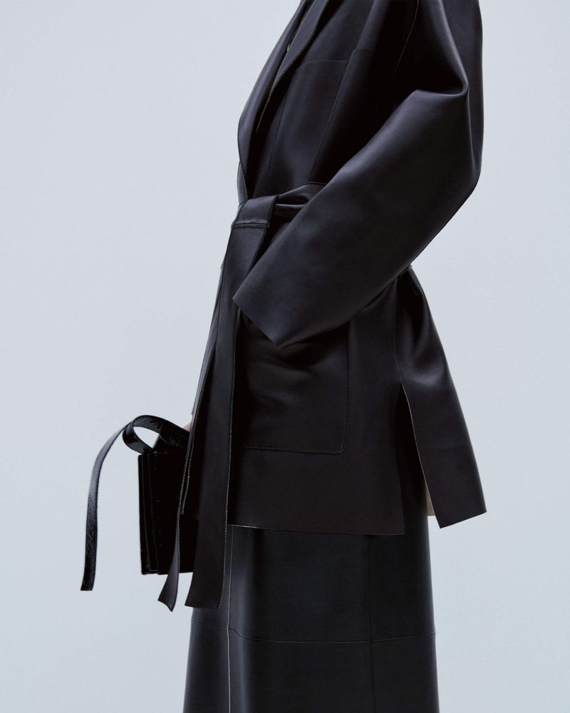 Leather blazer and skirt fashion shoot. A woman wears a black leather blazer with a tie waist and a matching midi skirt.