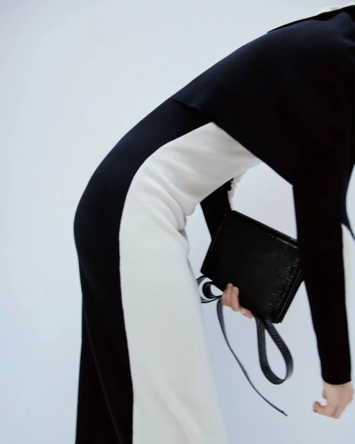 Fashion shoot features a woman in a monochrome jumpsuit holding a black clutch, set against a bright backdrop.