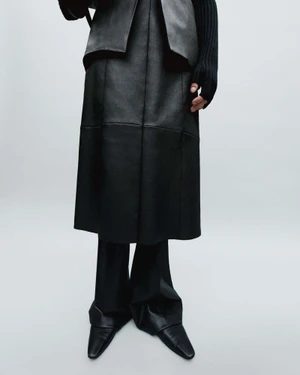 Model wearing a black leather panel skirt and trousers against a neutral grey studio backdrop
