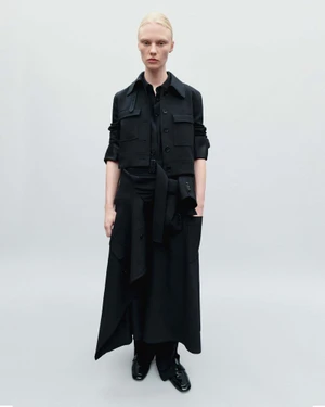 Model wearing a black belted coat and shirt against a seamless grey background