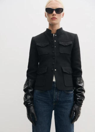 Model wearing black sunglasses, a structured black button-up jacket, and long black leather gloves against white backdrop