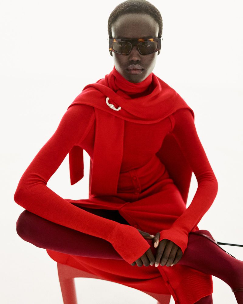 Fashionable adult female with sunglasses in a red outfit poses against a white backdrop in a studio shot.