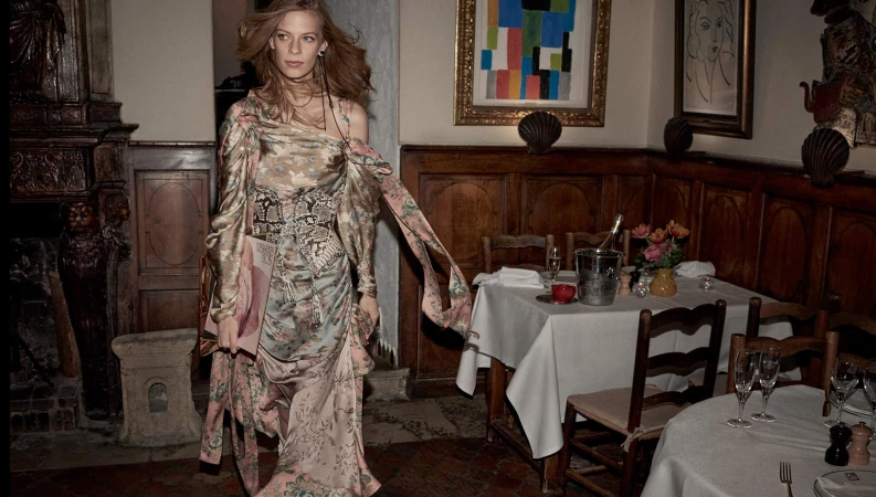 Model Lexi Boling in a patterned silk dress walking through a restaurant interior for Zimmermann