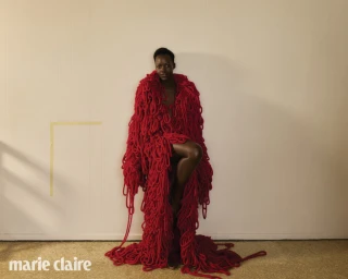 Lupita Nyong'o wearing a heavy textured red knitted coat standing against a light background for Marie Claire Australia