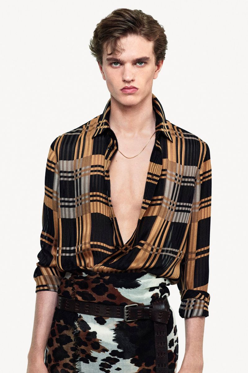 Model wearing a patterned plaid shirt and animal print skirt against a white studio background