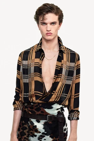 Model wearing a patterned plaid shirt and animal print skirt against a white studio background