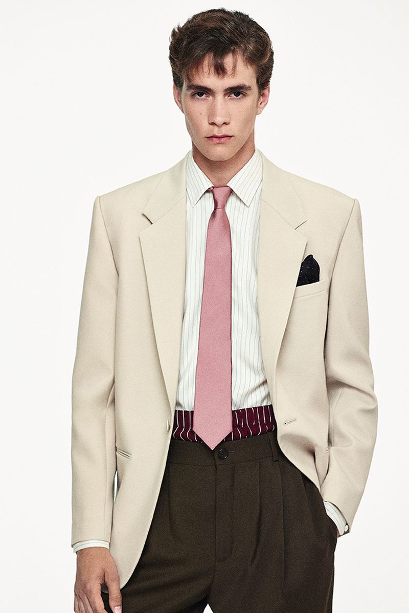 Adult man in a tan suit with a pink tie and a striped shirt, posing in front of a white background in a portrait shot.