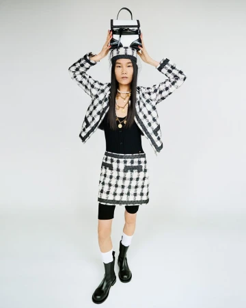 Model balancing a handbag on her head while wearing a black and white plaid skirt suit against a white background