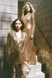 Two female models in glittering gold sequin outfits posing on outdoor stone stairs in a fashion campaign by Amanda Charchian.