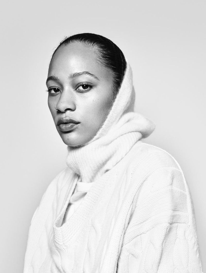 Monochrome portrait of an adult woman with dark hair and light skin wearing a white sweater against a neutral background.