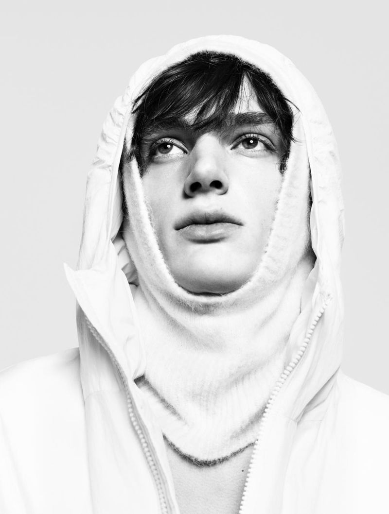 Close-up portrait of a male model wearing a white hooded jacket with zipped collar against a seamless white background.