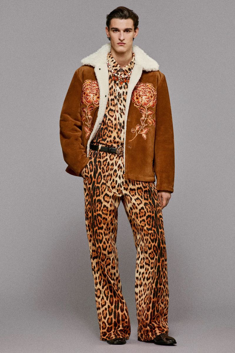 Male fashion model poses in a leopard-print ensemble, accented by a brown shearling jacket with embroidered floral detail.