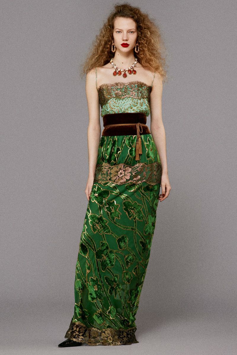 Model with voluminous curly hair wearing a strapless green patterned dress against a grey backdrop