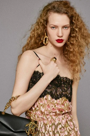 Fashion portrait of a curly-haired model wearing black lace and a gold dress with gold earrings, rings and a leather purse.