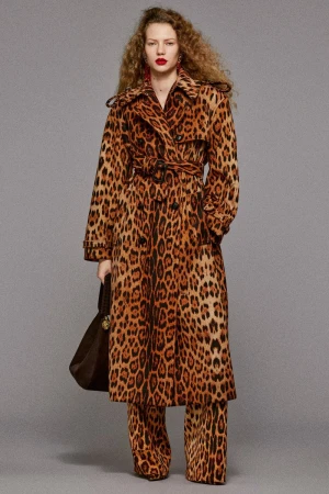Model wearing a matching leopard print trench coat and trousers holding a dark handbag against a grey backdrop