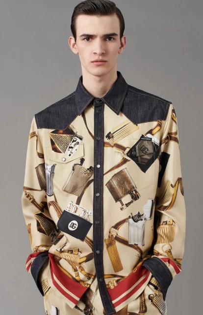 Male fashion model wears a patterned beige button-down shirt with denim shoulders in a studio shot against a neutral gray background.