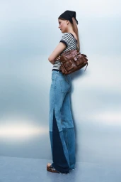 Model wearing a black headscarf, striped t-shirt, and blue jeans, carrying a brown leather shoulder bag against a grey backdrop.
