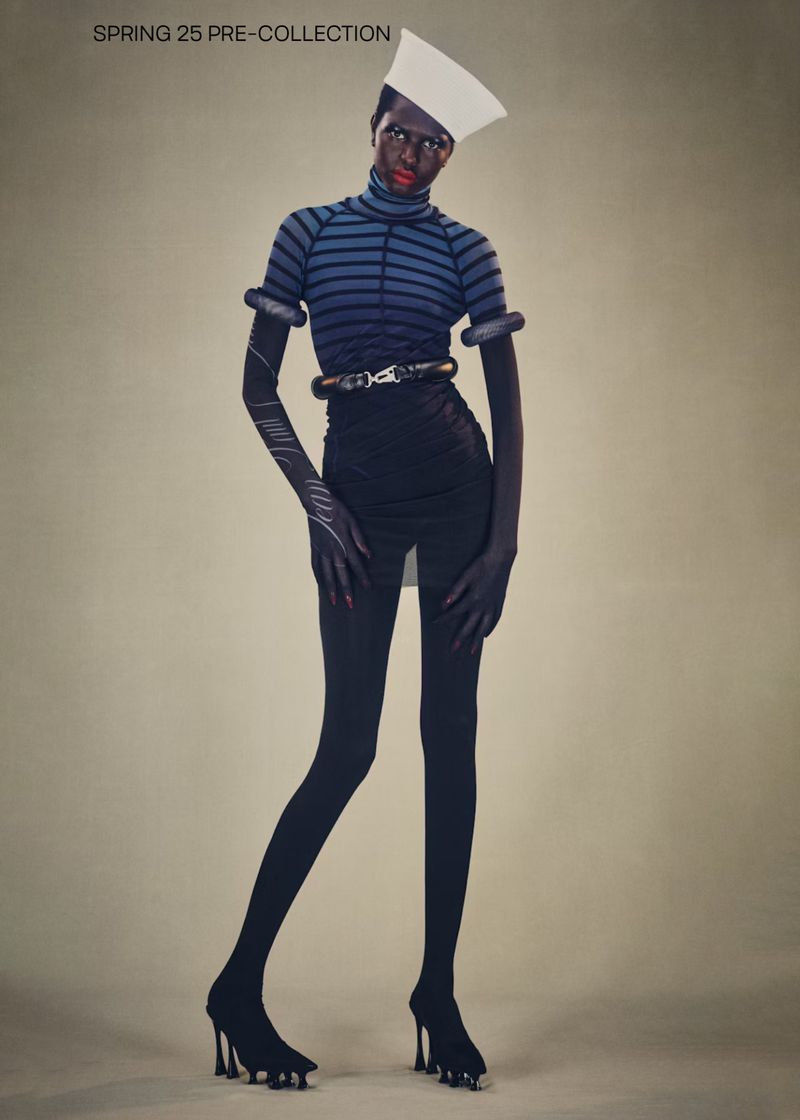 Fashion-forward full shot of a Black model in an avant-garde striped top, sculptural accessories, black skirt, tights, and platform heels.