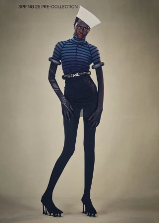 Fashion-forward full shot of a Black model in an avant-garde striped top, sculptural accessories, black skirt, tights, and platform heels.