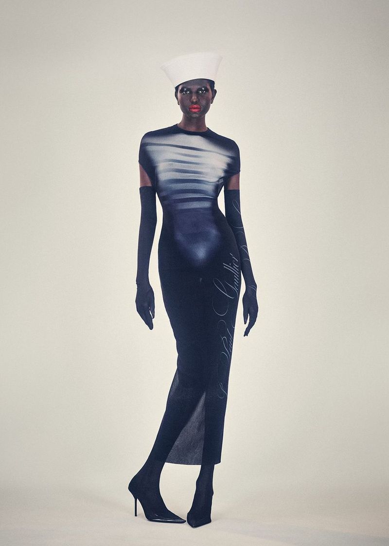 A striking fashion portrait featuring a dark-skinned model in a black and white dress, complete with matching gloves, heels, and a unique white hat.
